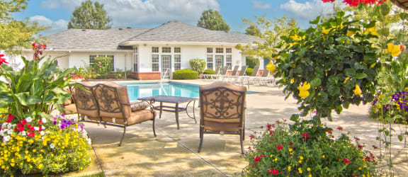 a backyard with a pool and patio furniture and flowers