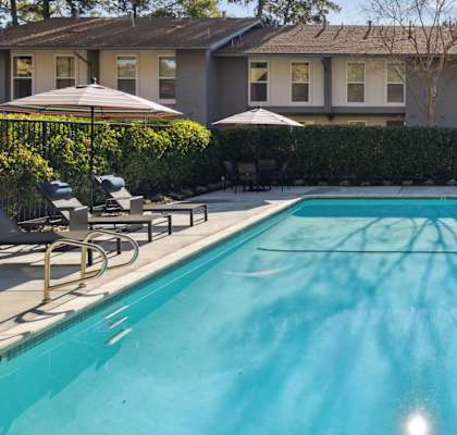 A swimming pool in front of a house with a blue sky and trees in the background.