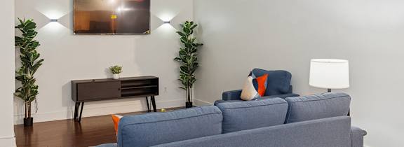 A grey couch sits in a white room with a wooden floor and a painting on the wall.
