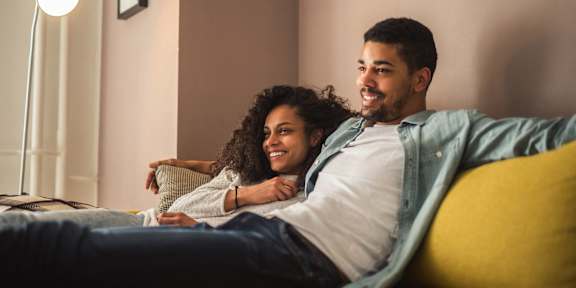 A couple is sitting on a yellow couch, smiling and enjoying each other's company.