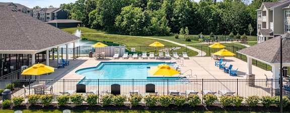 A large swimming pool surrounded by yellow umbrellas and blue loungers at Aventura at Wentzville I & II Apartments, Wentzville, MO, 63385