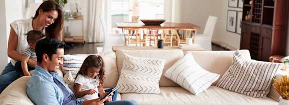 A family of three is sitting on a white couch in a living room.