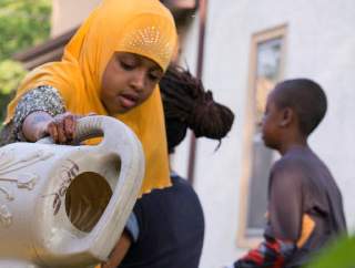 A woman in a yellow garment is pouring water from a white container.