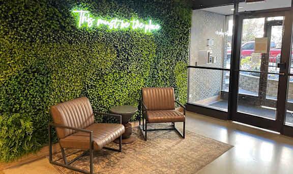 Two leather chairs are placed in front of a green wall with a neon sign that says "The master key".