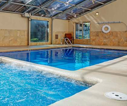 The turquoise indoor pool with tables, chairs, and windows with a glass ceiling at Retreat at Austin Bluffs Apartment Homes. 