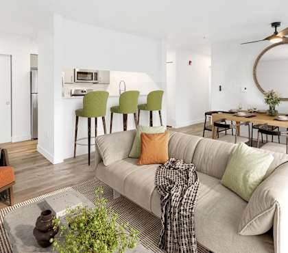 A living room with a white couch, orange chair, and a dining table with chairs.