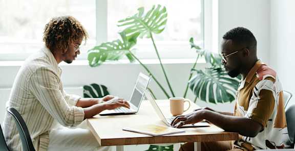 Two people working on laptops in a bright room.