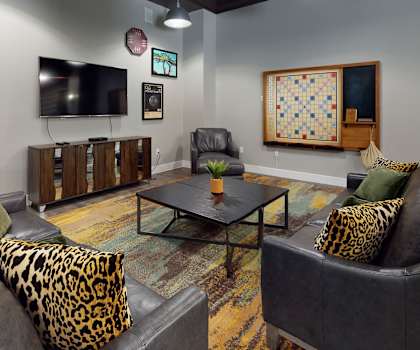 The front office and resident lounge with leather couches, a game board, a TV, and a coffee table at Lofts at Watter Creek Apartments. 