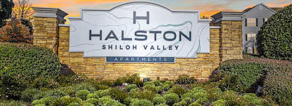 The Halston Shiloh Valley Apartments sign is displayed in front of a beautiful sunset.