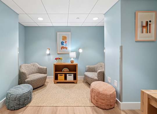 A room with blue walls and a wooden floor with a chair, ottoman, and table.