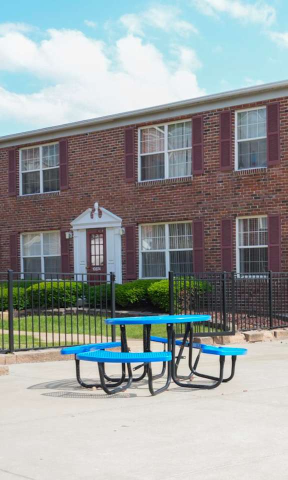 A red brick building with a white door and windows, a black fence, and a blue picnic table.