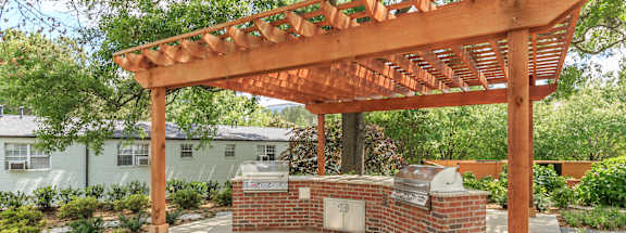 a backyard with a brick barbecue and a wooden pergola