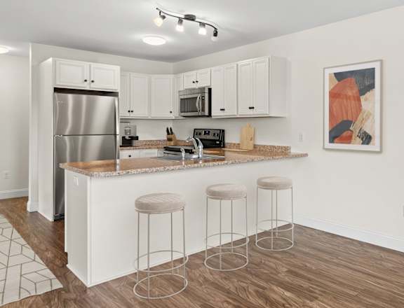 A kitchen with white cabinets and a white island with bar stools.