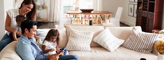 A family of three is sitting on a white couch in a living room.