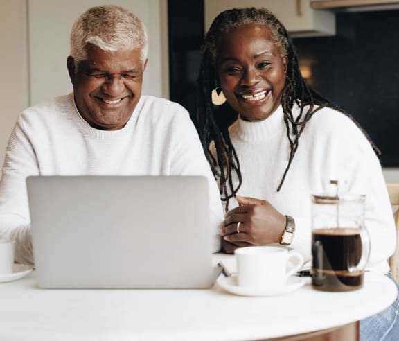 two people sitting at a kitchen table looking at a laptop computer