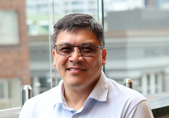 A man wearing glasses and a white shirt is leaning on a railing.