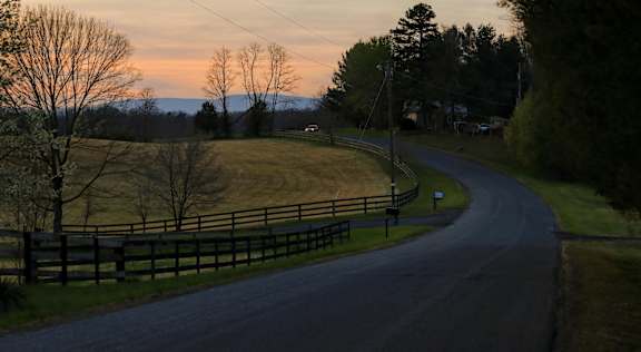 A road with a fence on the side and trees on the other side.