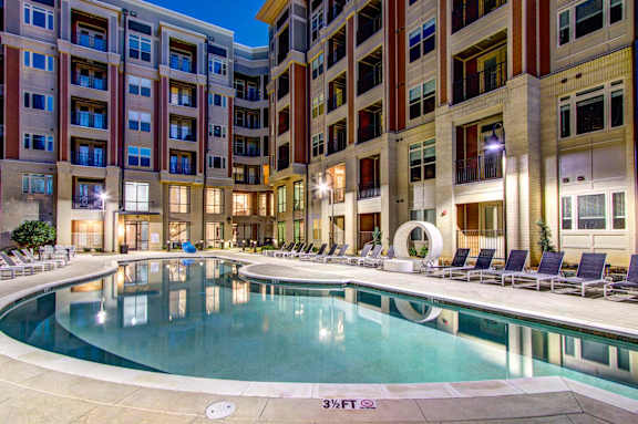 A swimming pool in front of a building with lounge chairs around it.