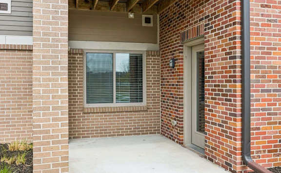 Covered patio with brick exterior walls, private entry door, and window overlooking the community courtyard.