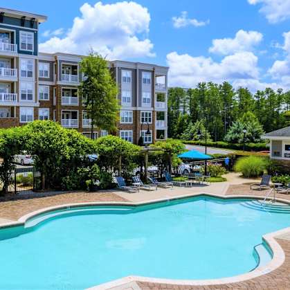 A swimming pool surrounded by lounge chairs and trees in front of apartment buildings.
