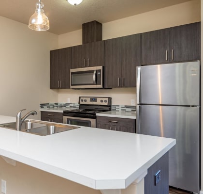Claxter Park Apartments | Interior kitchen with white quartz countertops, stainless steel refrigerator, stove and upper microwave. Blue and grey backsplash tile. Dark lower and upper cabinetry.