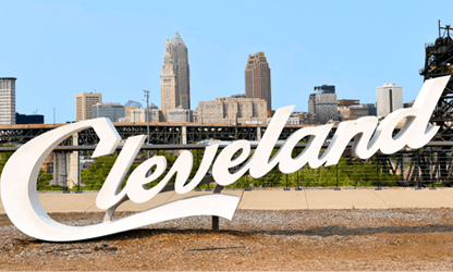 A large white sign with the word Cleveland on it in front of a city skyline.