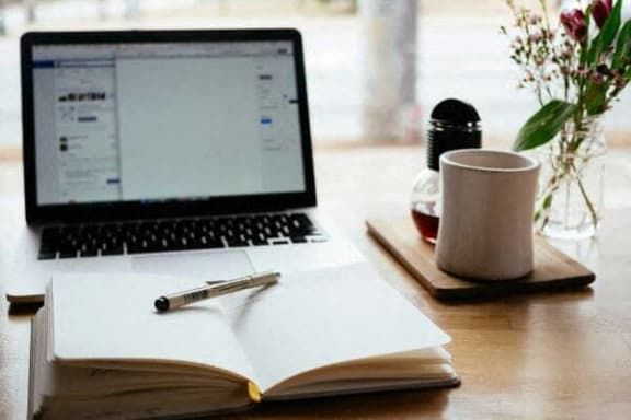 a laptop computer sitting on a desk with a notebook and a coffee cup