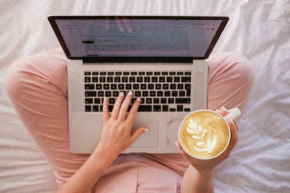 a woman sitting on a bed with a laptop and a cup of coffee