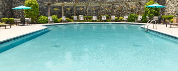 a swimming pool with lounge chairs and umbrellas in front of an apartment building at Chesapeake Ridge, Maryland