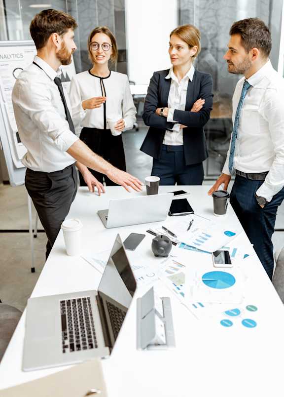 Four business people having a meeting around a table with laptops and papers.