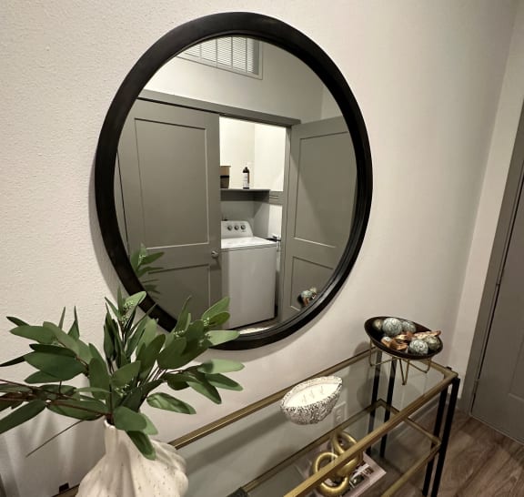 a round mirror above a glass table with a vase on it at The Depot, Raymore, MO