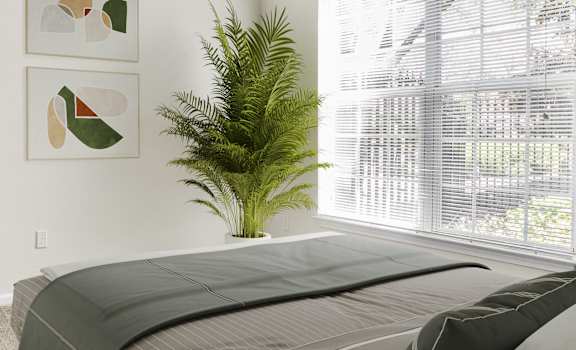 A bedroom with a bed, a plant, and two framed pictures on the wall.