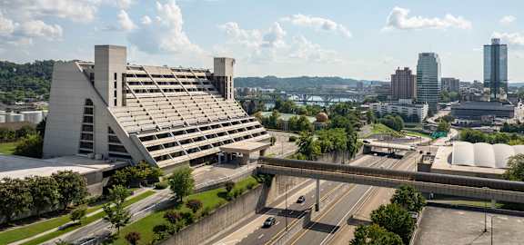 A modern building with a unique design is surrounded by a highway and other buildings.