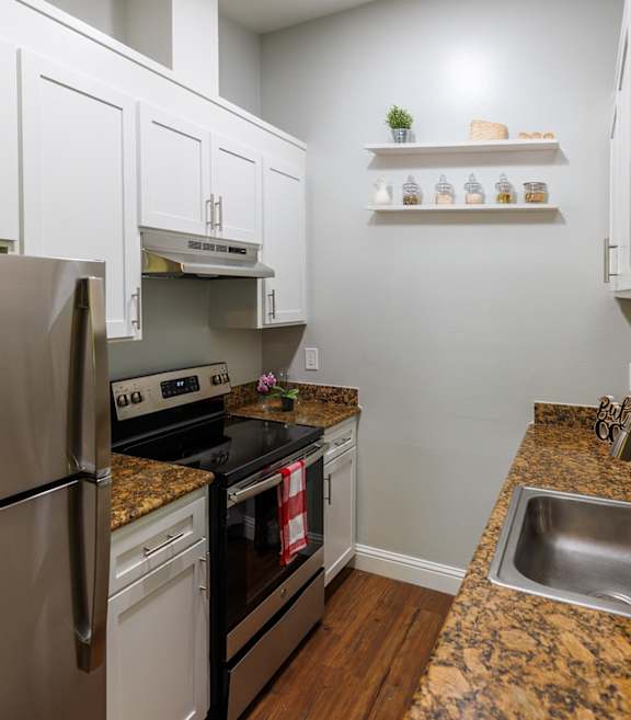 A kitchen with a stainless steel refrigerator, a granite countertop, and a sink.