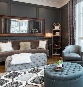 A living room with a grey ottoman, grey armchair, and a grey couch with a white throw.