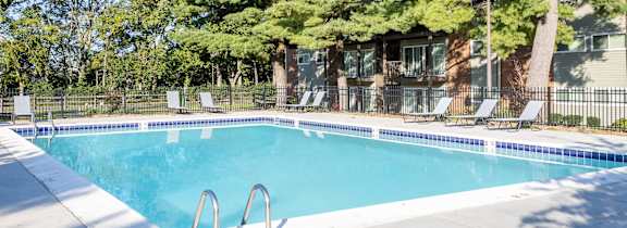 A swimming pool surrounded by trees and chairs.