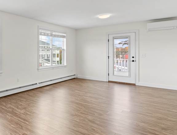A room with a white door and a window with a view of a house and trees.