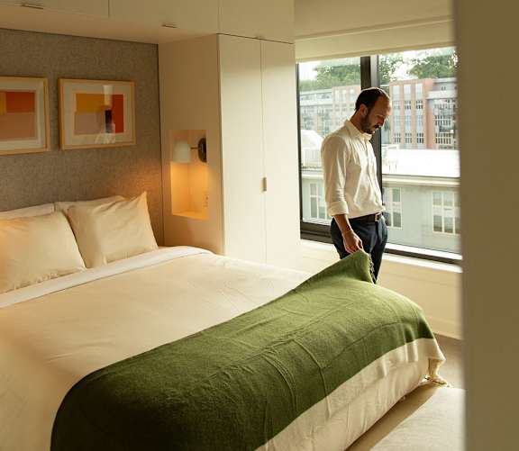 A man is standing in a bedroom with a green blanket on the bed. at Scout Living, powered by Placemakr Apartments, Atlanta, GA, 30308