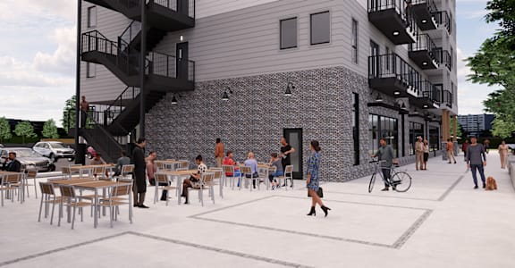 A group of people are sitting and standing on a patio outside a building with balconies.
