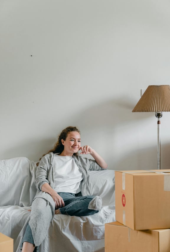 a woman sitting on a bed next to a pile of cardboard boxes