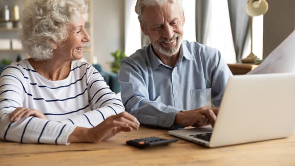 an older couple sitting at a table looking at a laptop