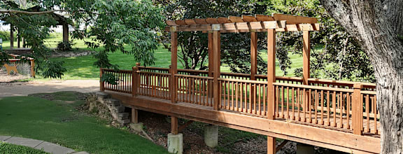 A wooden bridge over a grassy area with trees in the background.