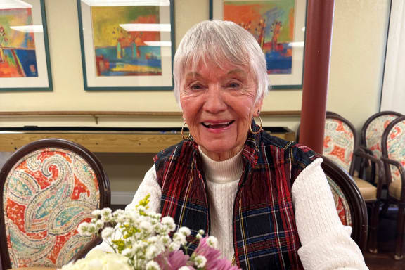 an older woman sitting at a table with a vase of flowers