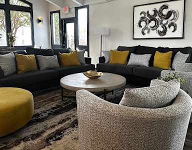 A modern living room with a grey couch, yellow ottoman, and a large abstract painting on the wall.