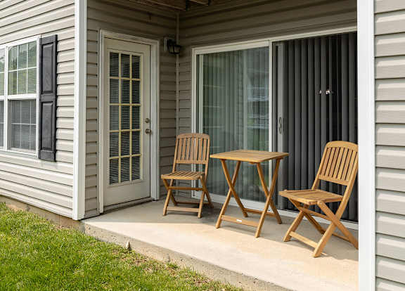 A wooden table and two chairs are on a porch.