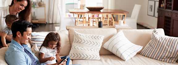A family of three is sitting on a white couch in a living room.