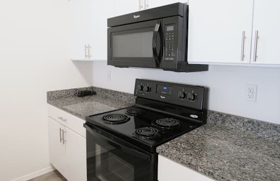 A black microwave oven is mounted above a black stove in a kitchen.