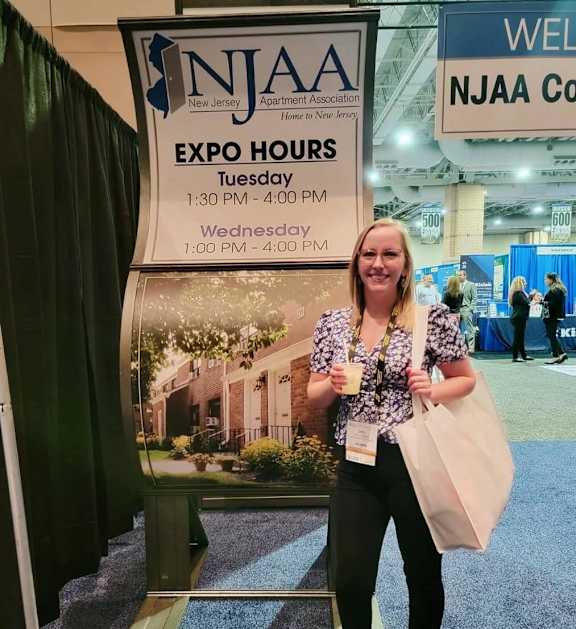 A woman stands in front of a sign for NJAA Expo Hours.