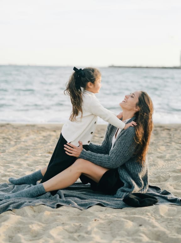 a woman sitting on the beach with a child on her back