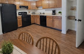 A living room with a black fridge and a wooden floor.